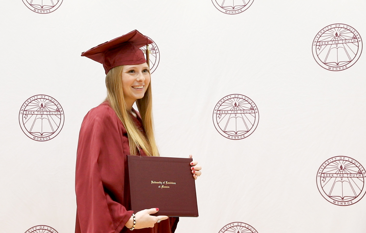 Graduate Photo Student smiling and posing with degree in front of backdrop at ceremony