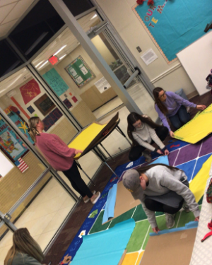 Literacy Lab students in a brightly colored classroom with floor mat featuring geometric shapes.