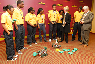 Students from the Carroll High School Robotics Team teach JPMorgan Chase Northeast Louisiana Market President Susan Hoffmann, and ULM President Dr. Nick J. Bruno how to navigate the robots programmed by the students. Photo of students and robotics